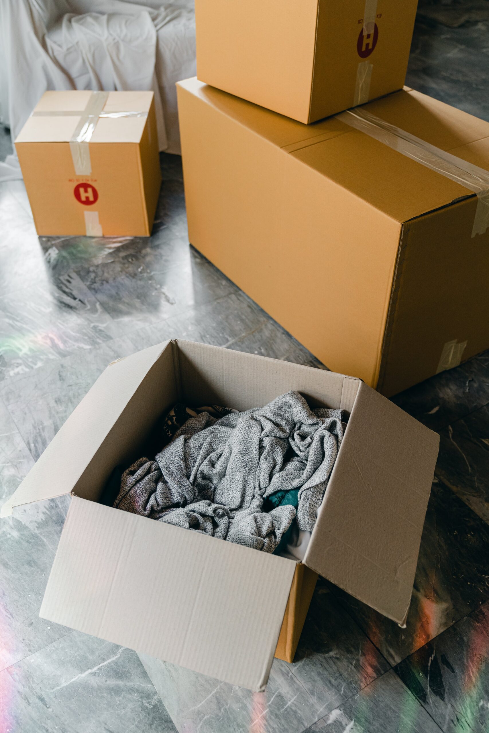 Moving boxes with clothes in them on a marble floor.
